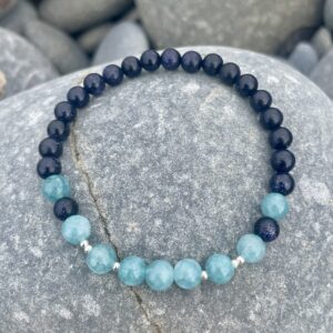 Aquamarine and Blue Sandstone Beaded Bracelet shown on a beach pebble.