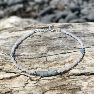 Delicate aquamarine and moonstone bracelet with sterling silver accents, displayed on a piece of driftwood to highlight its natural, coastal charm.