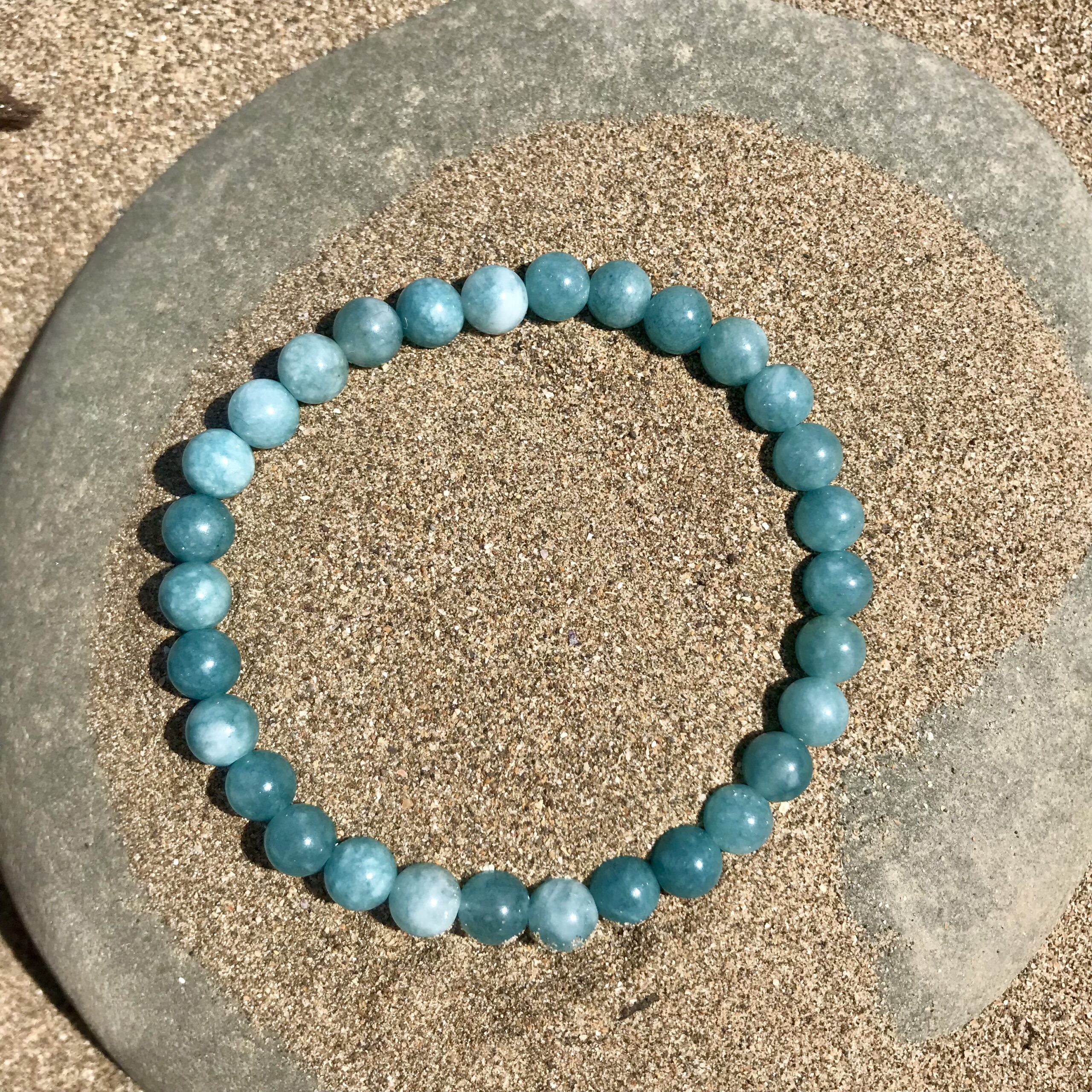 Simple aquamarine beaded bracelet with round gemstones, displayed on a beach background to highlight its soft blue tones and calming design.