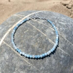Amarina aquamarine bracelet in sterling silver displayed on a pebble at the beach.