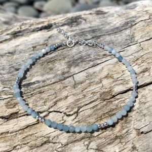 Aquamarine bracelet with sterling silver clasp and extender, a genuine gemstone bracelet laid out on driftwood by the ocean.
