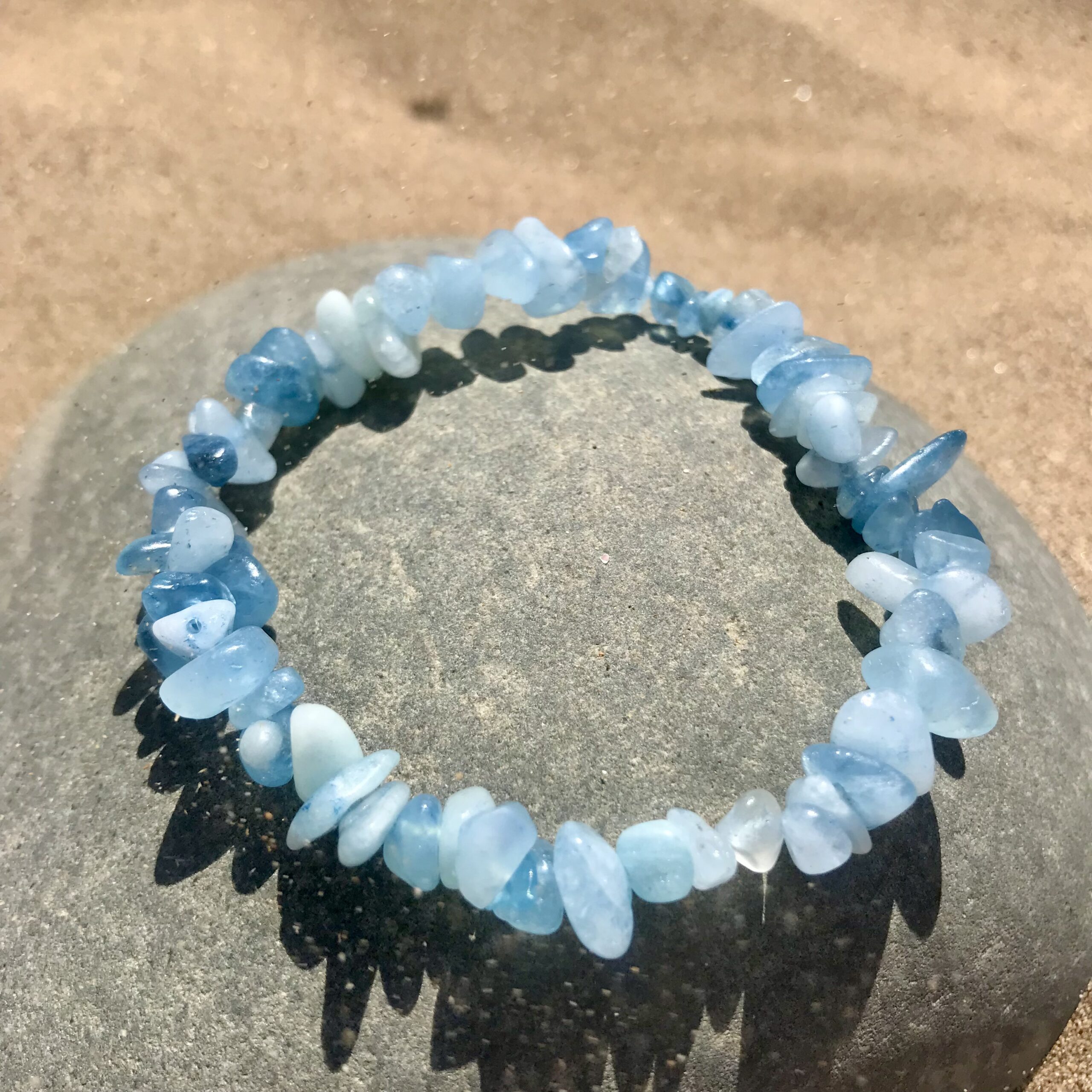 Raw aquamarine chip bracelet displayed on driftwood, highlighting its soft sea-blue tones and natural, organic texture.