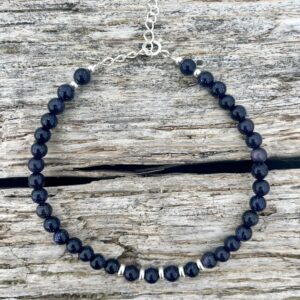 Harbour Blue Sandstone sterling silver bracelet resting on driftwood by the sea.