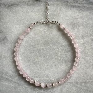 Close-up of rose quartz and silver bracelet on marble surface, feminine handmade bracelet with seaside charm.