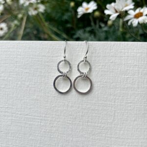 Hammered double circle sterling silver earrings, displayed outside with a background of daisys.