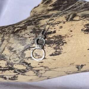 Hammered double circle sterling silver necklace resting on driftwood.