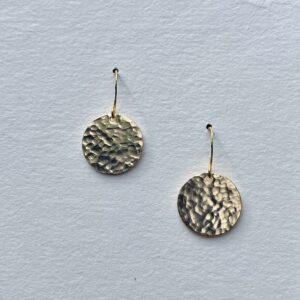 Hammered gold disc earrings catching the light.